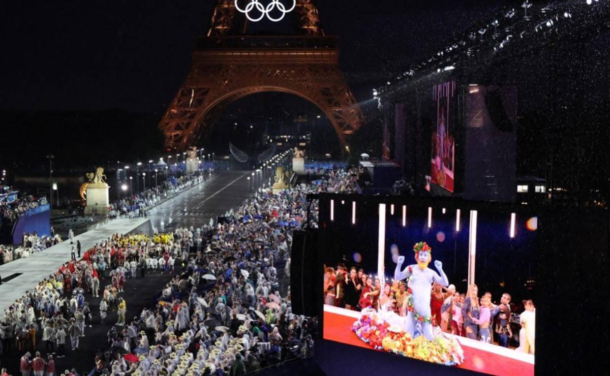 <i>Las delegaciones llegan al Trocadero mientras los espectadores observan al cantante francés Philippe Katerine actuando en una pantalla gigante durante la ceremonia de apertura de los Juegos Olímpicos de París 2024 en París el 26 de julio de 2024, mientras se ve la Torre Eiffel de fondo. FOTO Ludovic MARIN / POOL / AFP</i>