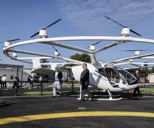 <i>Varias personas se encuentran junto a un taxi volador Volocopter Volocity en el aeródromo de Saint-Cyr-l'École, Francia, el 8 de agosto de 2024, para conmemorar la inauguración del primer vertiport, una pista de despegue y aterrizaje para taxis. Foto de Thibaud MORITZ/AFPThibaud MORITZ / AFP</i>