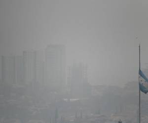 <i>Una bandera nacional hondureña ondea en medio de una densa capa de humo que cubre Tegucigalpa el 6 de mayo de 2024. La capital hondureña enfrenta problemas de contaminación debido a la gran cantidad de vehículos e incendios forestales que ocurren en la región. FOTO Orlando SIERRA/AFP</i>