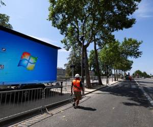 <i>Un trabajador pasa junto a una pantalla gigante que muestra el logotipo de Microsoft, para la ceremonia de apertura de los Juegos Olímpicos de París 2024 en una zona gris en París el 19 de julio de 2024.FOTO EMMANUEL DUNAND/AFP</i>