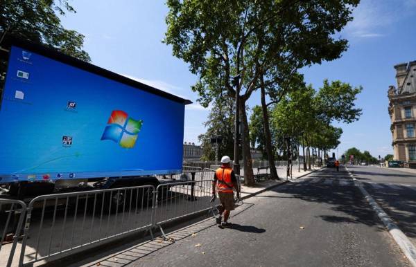 <i>Un trabajador pasa junto a una pantalla gigante que muestra el logotipo de Microsoft, para la ceremonia de apertura de los Juegos Olímpicos de París 2024 en una zona gris en París el 19 de julio de 2024.FOTO EMMANUEL DUNAND/AFP</i>