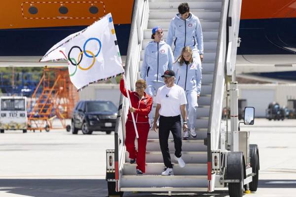 <i>La alcaldesa de Los Ángeles, Karen Bass (abajo a la izquierda), ondea la bandera olímpica junto al presidente de LA28, Casey Wasserman (abajo a la derecha), la saltadora de trampolín estadounidense Delaney Schnell (centro a la derecha), el patinador estadounidense Tate Carew (2.º a la izquierda) y el jugador de voleibol estadounidense Micah Maʻa (atrás) después de que su avión aterrizara durante un evento que celebraba la llegada de la bandera olímpica al Aeropuerto Internacional de Los Ángeles (LAX) en Los Ángeles, el 12 de agosto de 2024. Los Ángeles albergará los Juegos Olímpicos de Verano de 2028. FOTO Etienne LAURENT / AFP</i>